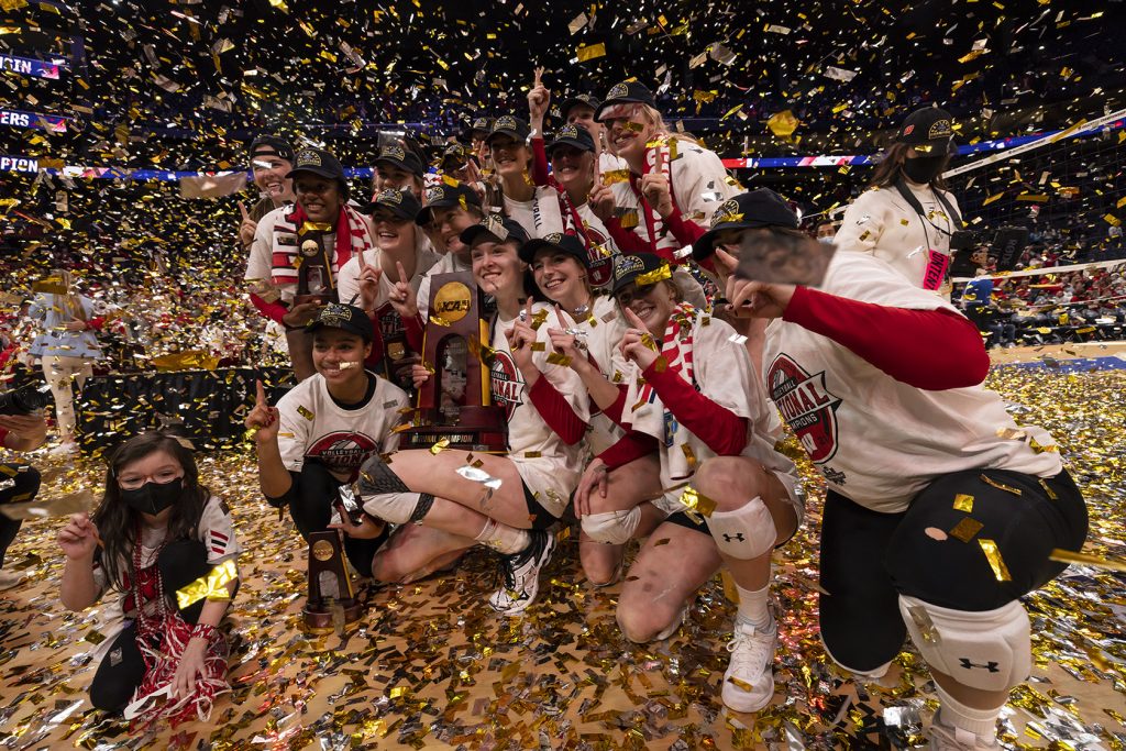The UW Women's Volleyball team pose for photos on the court holding their 2021 NCAA Championship trophy as confetti rains down