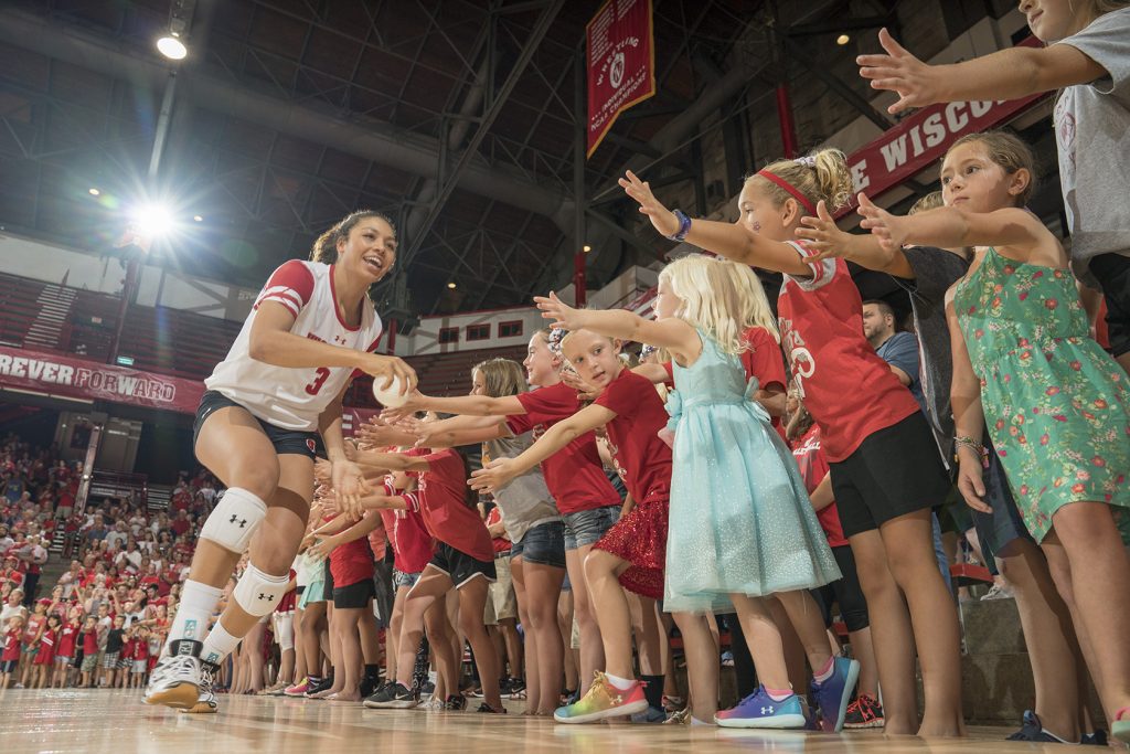 A member of the UW Women's Volleyball team gives high fives to a row of young fans