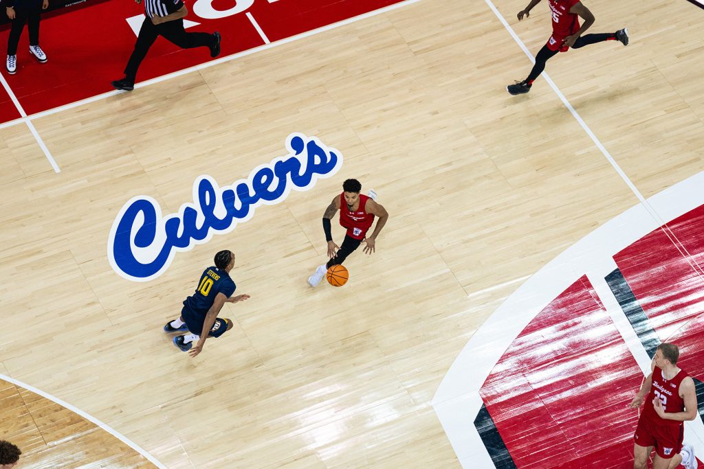 A member of the UW Men's basketball team dribbles the ball across the Kohl Center court which sports a "Culver's" logo