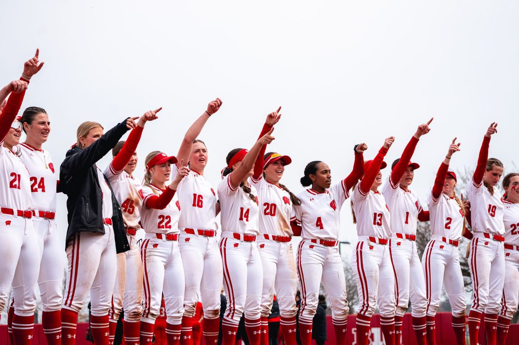 Members of the UW Women's Softball team stand in a row and sing "Varsity" with their arms raised
