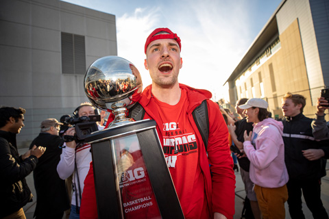 A Badger men's basketball player holds the Big Ten Championship trophy outside on campus.