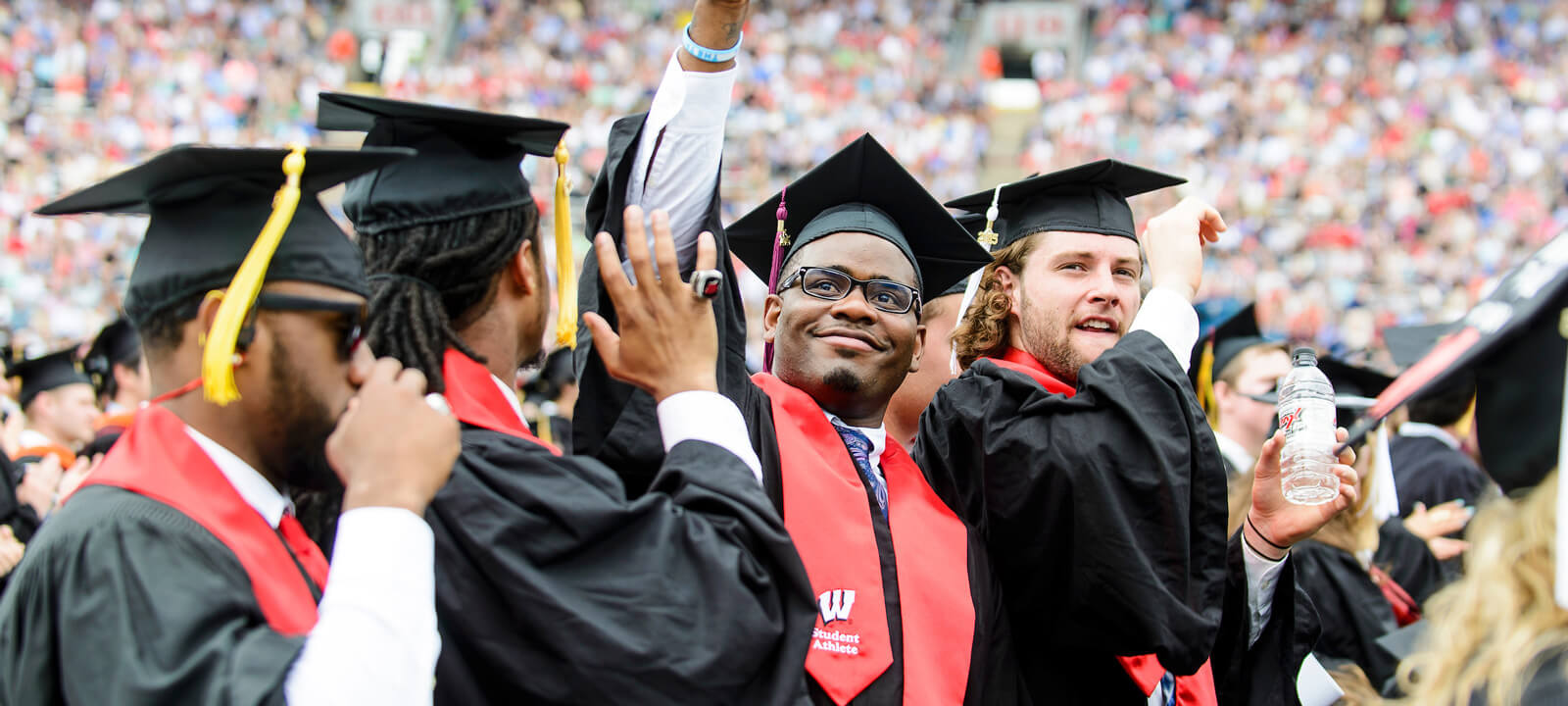 Graduating student-athletes smile and show off their diplomas at the outdoor graduation ceremony in Camp Randall Stadium.