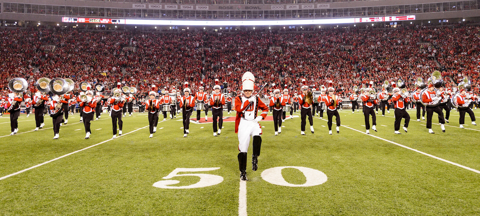 UW Marching band aligned and facing the camera during a football game, a full stadium of Badger fans behind them.